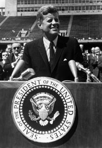 JFK standing at a podium with the seal reading: The President of the United States