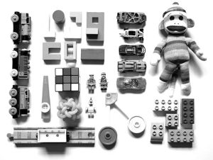 an array of different pieces of toys laid out on a white background: legos, rubik's cube, a kazoo, and others.