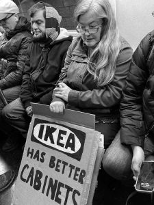 Woman sitting with a protest sign that reads "IKEA has better cabinets"