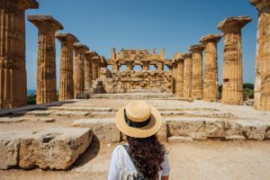 Person standing in front of historic ruins in the desert, wearing a hat