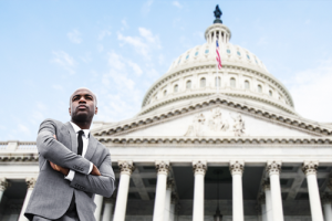 Person with arms crossed, standing in front of the U.S. capitol building.