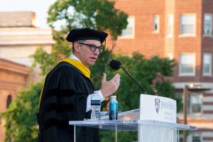 Clint Watts at the podium, giving 2024 commencement speech at Homewood Field on the JHU campus in Baltimore, Maryland