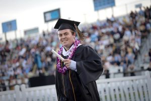 Graduate smiling in cap and gown, holding diploma