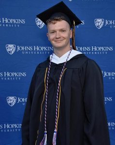 Codee Potts in cap and gown standing in front of Johns Hopkins University backdrop.