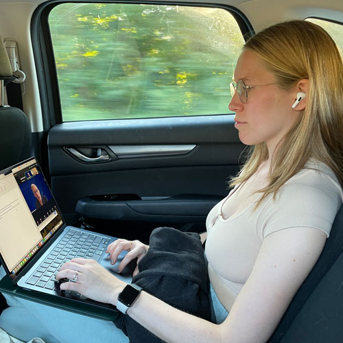 Natalia Duane working on her laptop in the backseat of a moving vehicle.