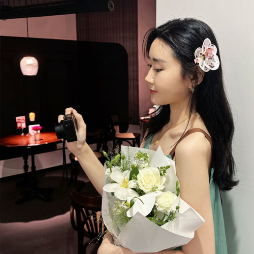 Yujie Tian holding a bouquet of flowers in one hand and a camera in the other.