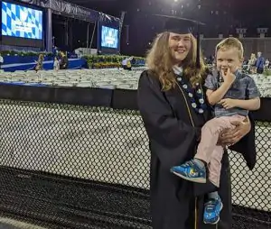 Alumni ambassador holding their child at the graduation ceremony