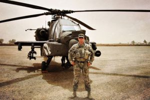 Joe Wankelman standing in cammo in front of a helicopter.